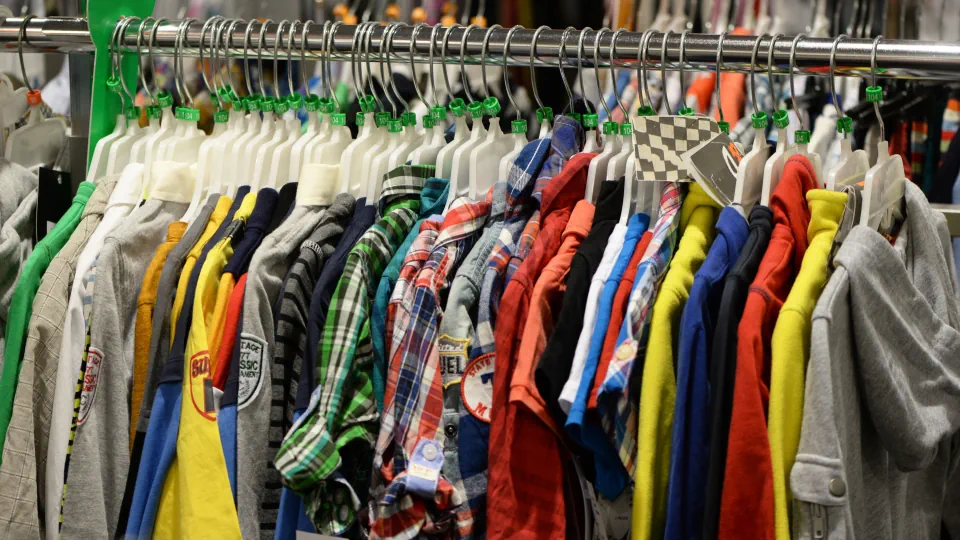 Klima-Wandel: Kleidungstücke hängen dicht an dicht an Bügeln in einem Geschäft.